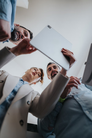 Colleagues gather around a tablet, looking down and smiling during a casual team moment in the officeの写真素材