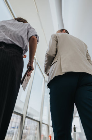 Business colleagues walk through a bright office corridor with a clipboard in handの写真素材