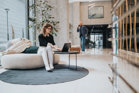 Business office lobby scene with woman on laptop and man talking on phone in backgroundの写真素材