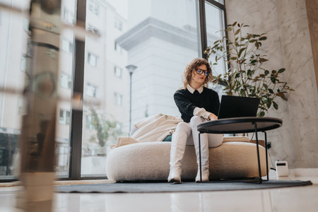 Professional woman works on laptop in a bright modern lounge with large windowsの写真素材