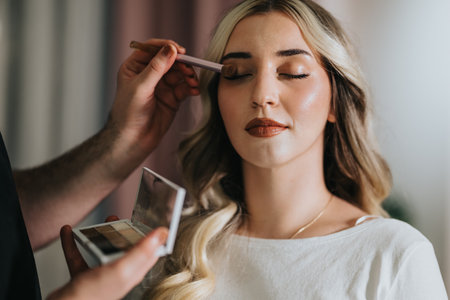 Makeup artist applies eyeshadow and lip color on a woman in a beauty studioの写真素材