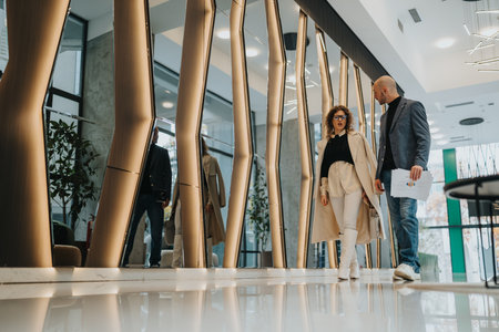 Business partners walk through a modern office lobby, discussing plans and sharing documentsの写真素材