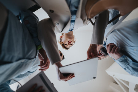 Colleagues gather around a tablet in a modern office, collaborating and sharing ideasの写真素材
