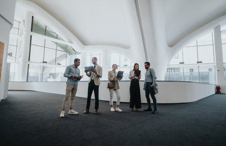 Group of colleagues in a modern office lobby discussing plans with tablets and documentsの写真素材