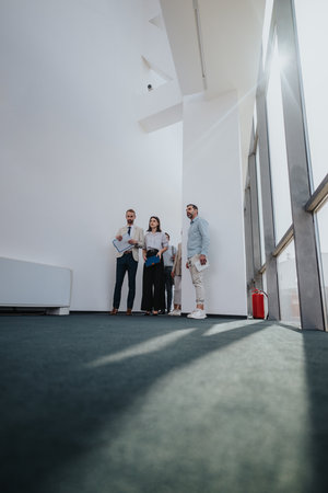 Group of colleagues in a modern office atrium discussing project details with documentsの写真素材