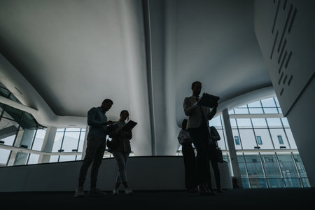 Silhouetted colleagues review documents in a modern, curved ceiling lobby during a business meetingの写真素材