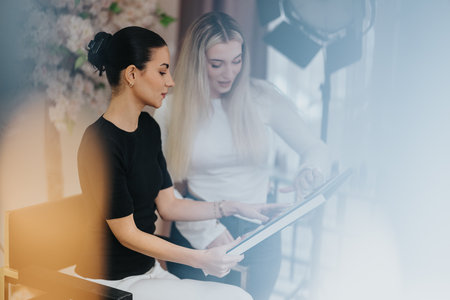 Two women review a tablet during a collaborative studio session, smiling and focusedの写真素材