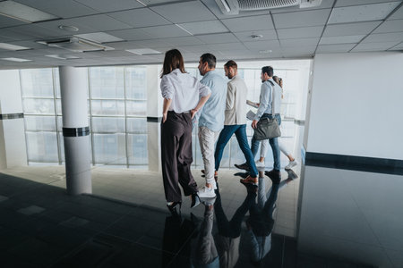 A group of colleagues walk through a modern office hallway, discussing work and heading to a meetingの写真素材