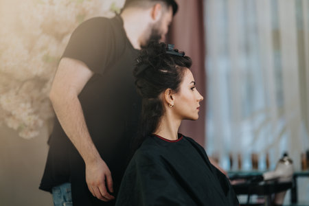 Woman sits for professional hair styling at a salon while the stylist works behind herの写真素材