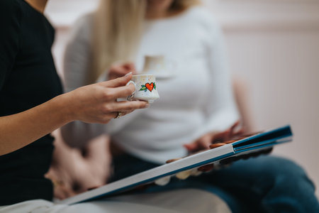 Friends sharing a coffee break while looking at a photo album in a cozy settingの写真素材