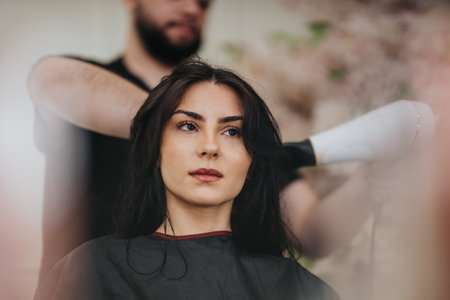 Woman receiving a professional hair styling at a salon with a focused expression and calm moodの写真素材
