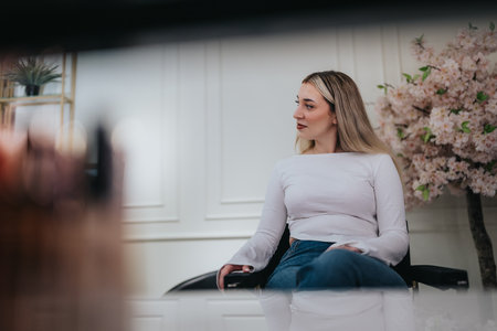 Woman in white top seated in a modern lounge with pink blossoms and soft lightingの写真素材