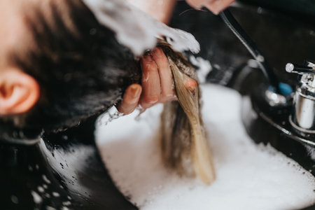 Hair wash at salon with bubbles and foam as hands shampoo and rinse at the sinkの写真素材