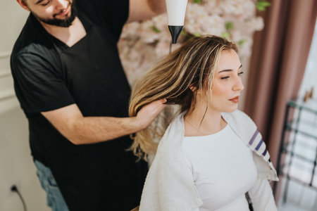 Hair stylist performs blow dry on client in a cozy salon settingの写真素材