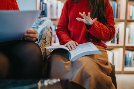 Two women in a cozy bookstore discuss a book as one reads and the other gesturesの写真素材