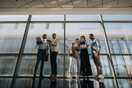 Group of professionals in a modern office discussing documents and plans in a glass-filled buildingの写真素材