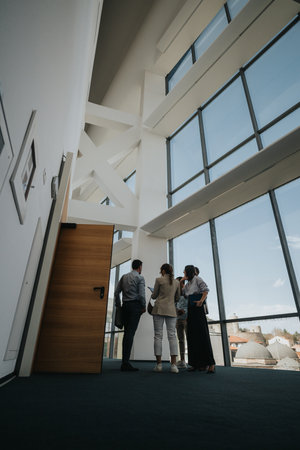 Group of colleagues in a modern atrium discussing ideas near expansive glass windowsの写真素材