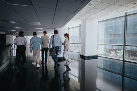 Group of colleagues walking through a modern office hallway with large windows and reflectionsの写真素材