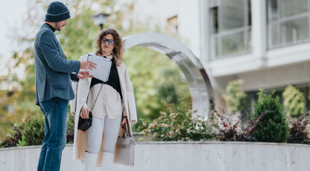 Business partners discuss documents outdoors in a modern urban plaza with stylish outfitsの写真素材