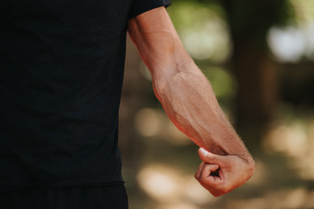 Close-up of a flexed arm with prominent veins in outdoor setting wearing black shirtの写真素材