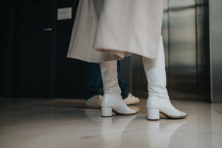 Stylish white knee-high boots in a modern indoor setting as two people walk togetherの写真素材