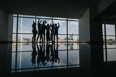 Group of coworkers celebrates victory in a modern office with city skyline backdrop and reflectionの写真素材