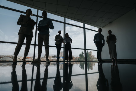Silhouetted group of colleagues in a modern office lobby with large windows, ready for a business meetingの写真素材