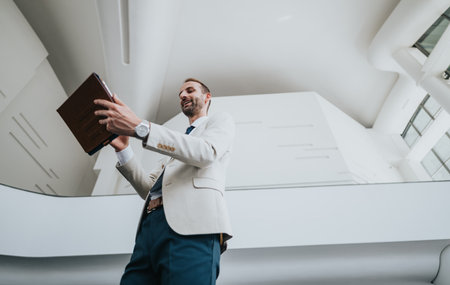 Businessman in a light suit holds a book in a modern office, delivering a confident presentationの写真素材