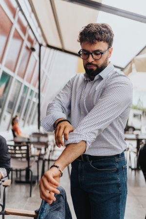 Man in casual attire rolls up sleeves in a modern outdoor cafe settingの写真素材