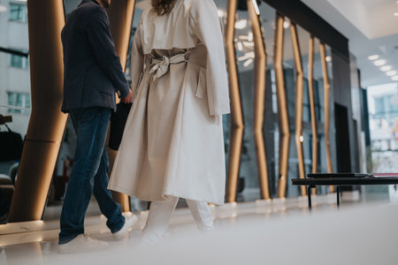 Business partners walk through a modern office lobby in stylish coats and casual attireの写真素材
