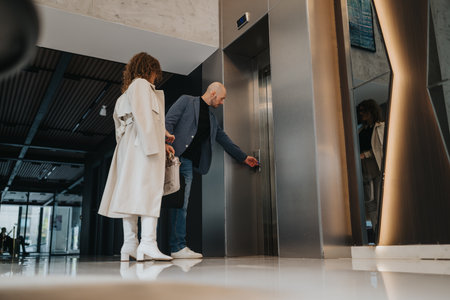 Business partners waiting by the elevator in a sleek, modern lobby before a meetingの写真素材
