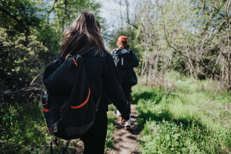 Two hikers with backpacks walk along a sunlit forest trail, enjoying the outdoorsの写真素材