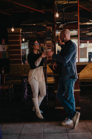Two colleagues toast drinks at a stylish, moody bar, sharing a friendly moment after workの写真素材
