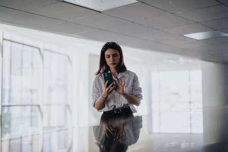 Woman using a smartphone in a bright office lobby, focused on screenの写真素材
