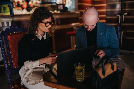 Two professionals collaborate at a cafe table with laptop and documents, engaged in a focused business discussion and planning sessionの写真素材