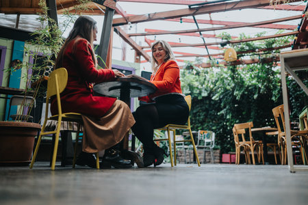 Two women enjoy a relaxed business meeting at an outdoor cafe in a vibrant courtyardの写真素材