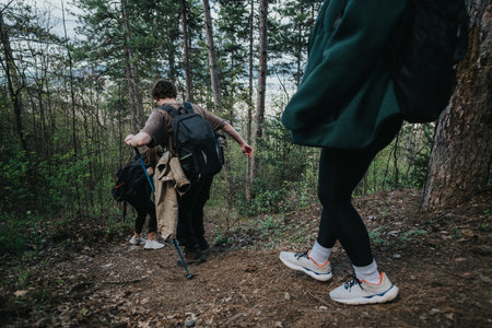Hikers trek down a forest trail with backpacks, trekking poles, and friends on a mountain hikeの写真素材