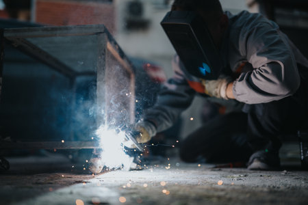 Welding worker in protective gear performs metal welding with bright sparks in a busy workshopの写真素材