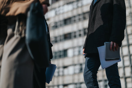 Two colleagues in business attire stand outdoors with folders and documents in an urban settingの写真素材