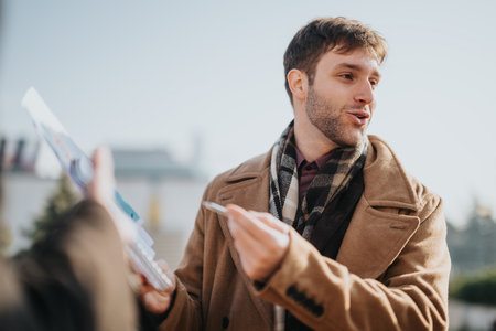 Man in brown coat and scarf presents a brochure during daytime outdoor exchangeの写真素材