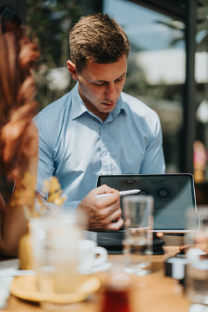 Business professional using tablet and stylus at an outdoor cafe during a collaborative meetingの写真素材