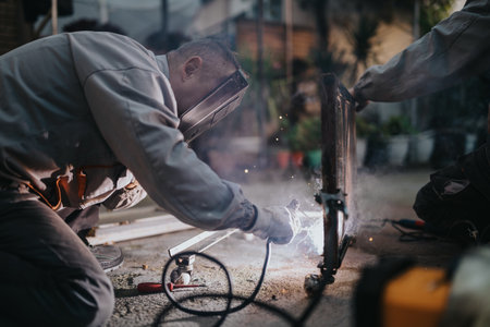 Outdoor welding work: a worker fusing metal with a grinder amid sparks and protective gearの写真素材