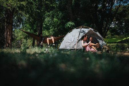 Family and friends relax at a campsite with a tent and hammock in a lush forest settingの写真素材