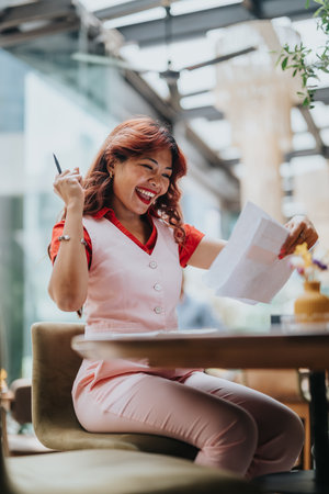 Happy woman in pink business outfit celebrates with documents and penの写真素材