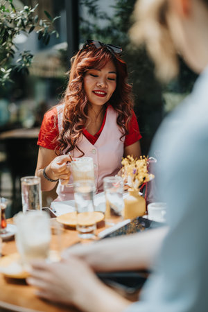 Outdoor cafe scene with a smiling woman pouring coffee for a friendの写真素材