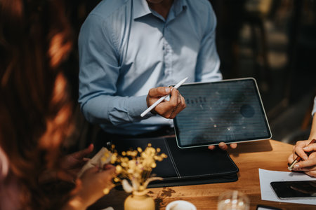 Business associates discuss strategy with a tablet and stylus at an outdoor cafe meetingの写真素材