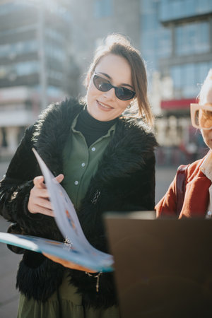Two women review documents outdoors in an urban city setting, smiling and collaboratingの写真素材
