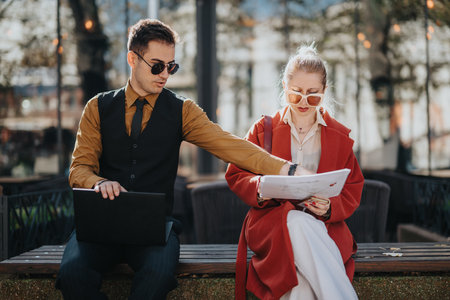 Business partners discuss plans on an urban bench with laptop and documentsの写真素材