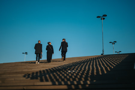 Young coworkers walk up steps on a sunny day, projecting teamwork and ambitionの写真素材