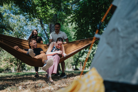 Friends and family relax in a hammock in the park during a sunny outdoor campの写真素材